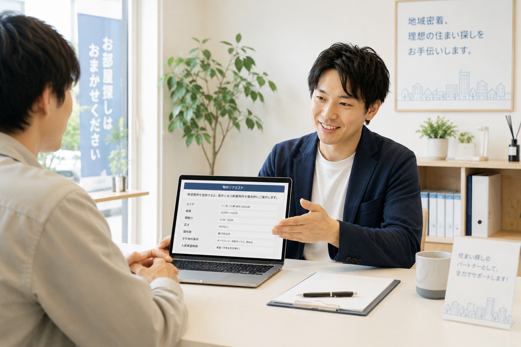 不動産会社の店舗でスタッフがパソコン画面を示しながら相談に乗る様子
